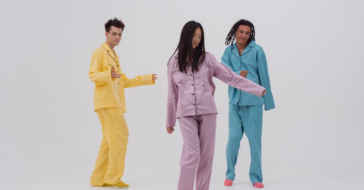 Three young adults wearing colorful pajamas dance joyfully on a white background.