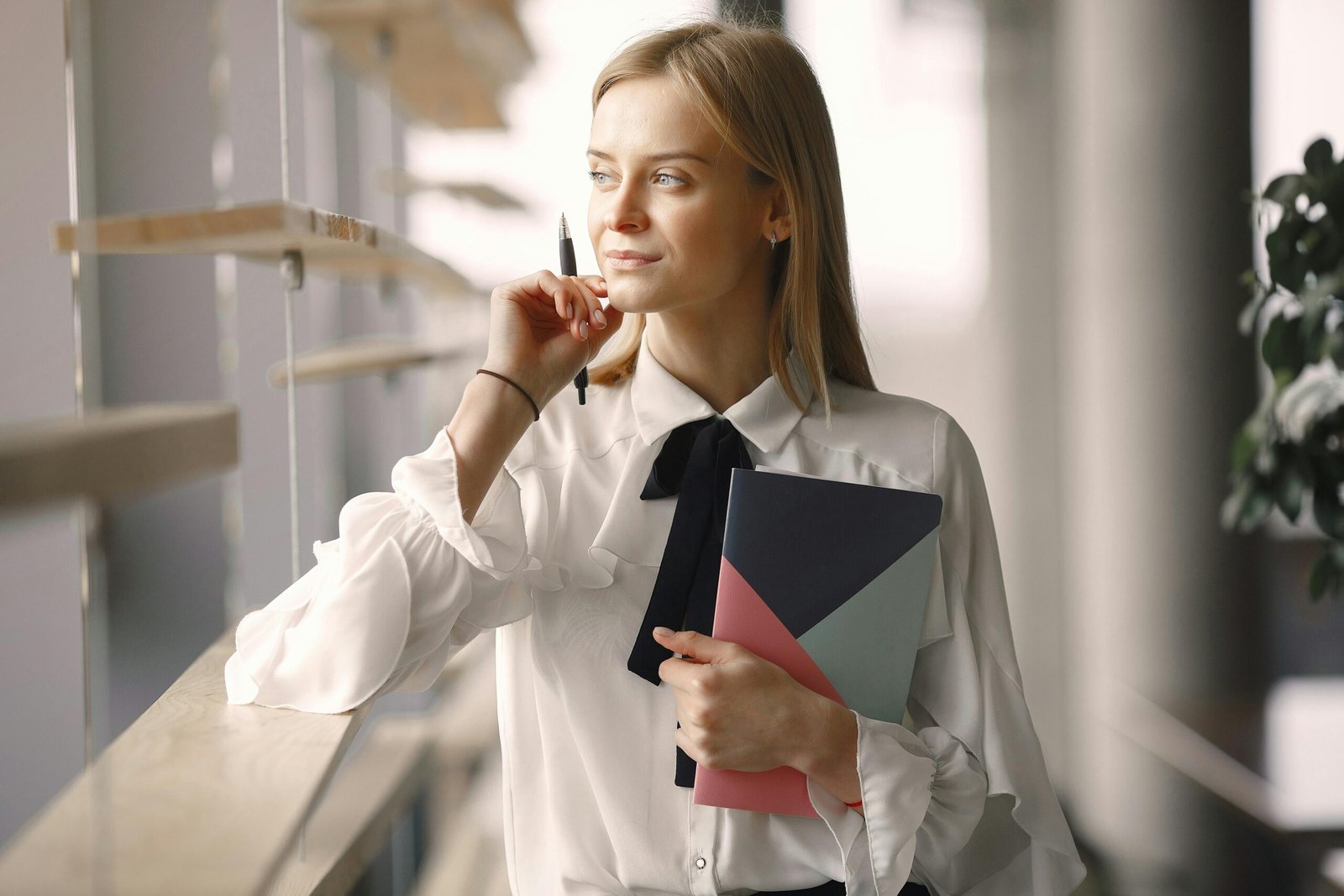 Elegant professional woman standing in a modern office, gazing thoughtfully out the window.