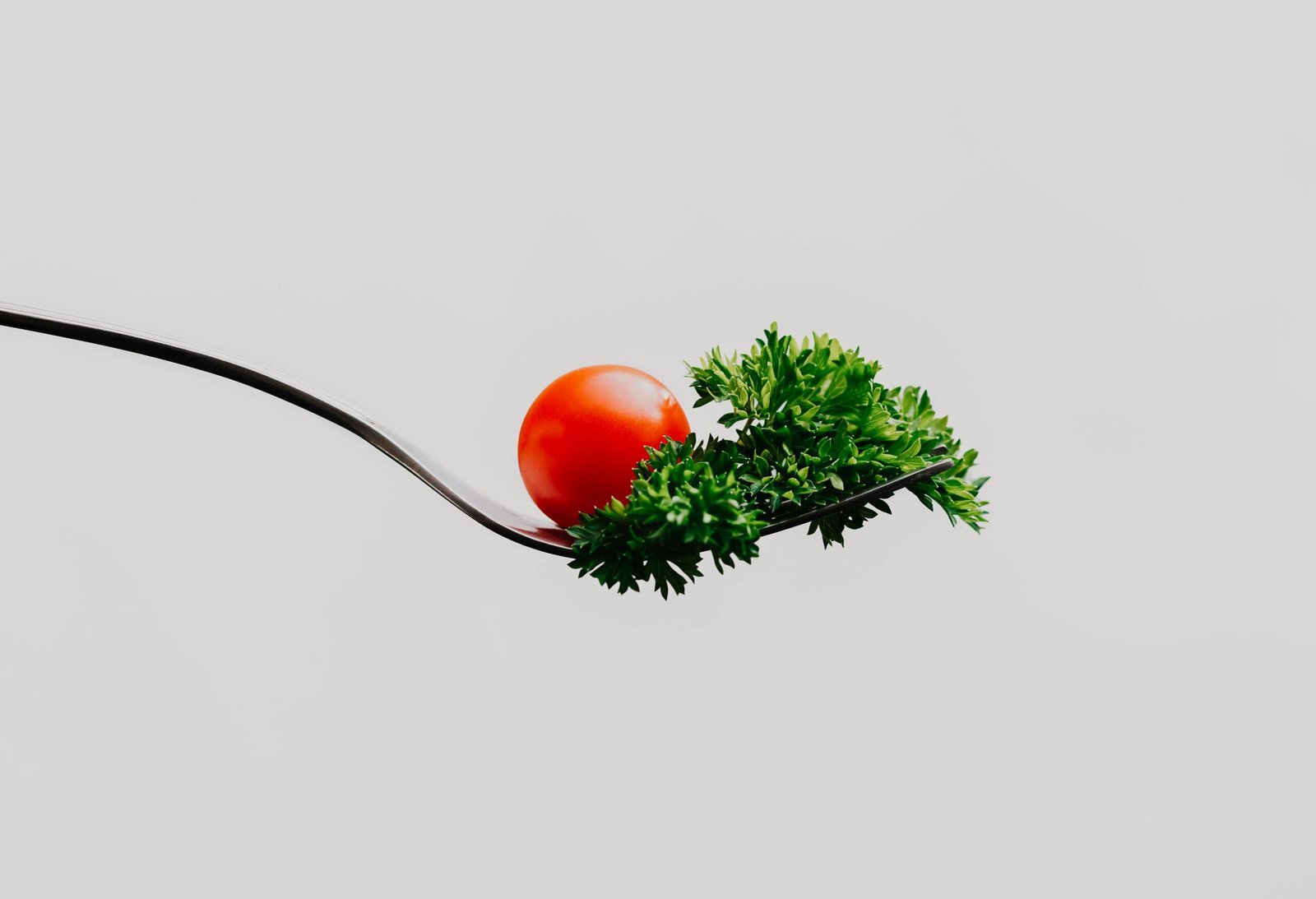 Minimalist close-up of a cherry tomato and parsley on a fork. Perfect for food design.